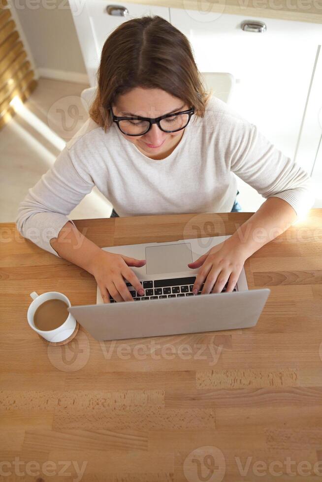 Top view of womans hands typing on laptop keypad wearing glasses and coffee on the table photo