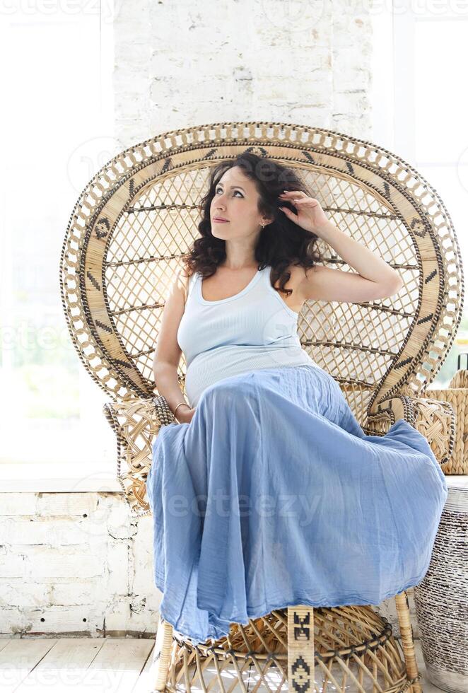 Pregnant woman resting in wicker armchair photo