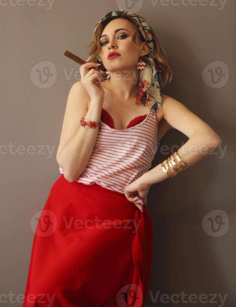 Portrait of beautiful woman in bright clothing and bow in head with bright lips holding cigar and smoking looking forward photo