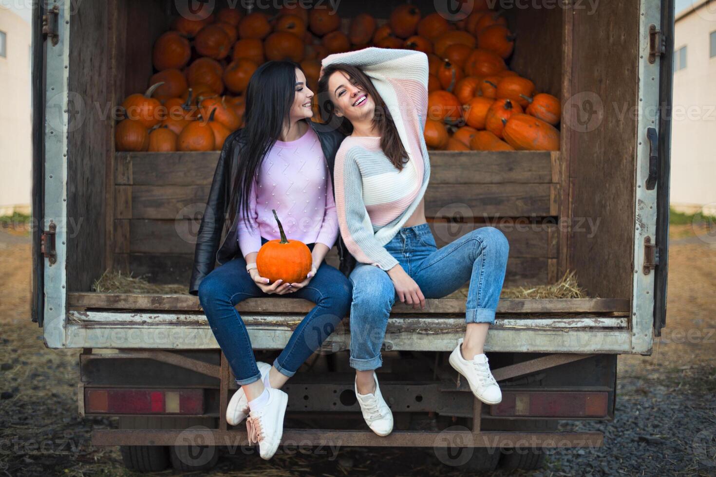 Fashionable beautiful young girlfriends together at the autumn pumpkin patch background. Having fun and posing photo