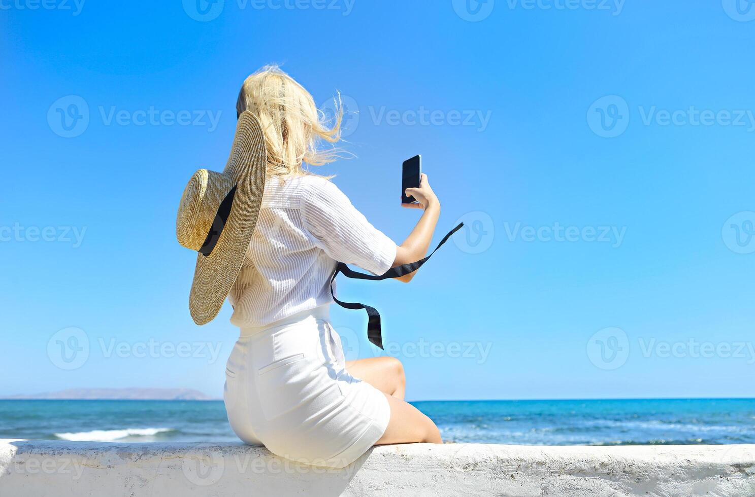 Unrecognizable blond woman taking selfie near sea photo