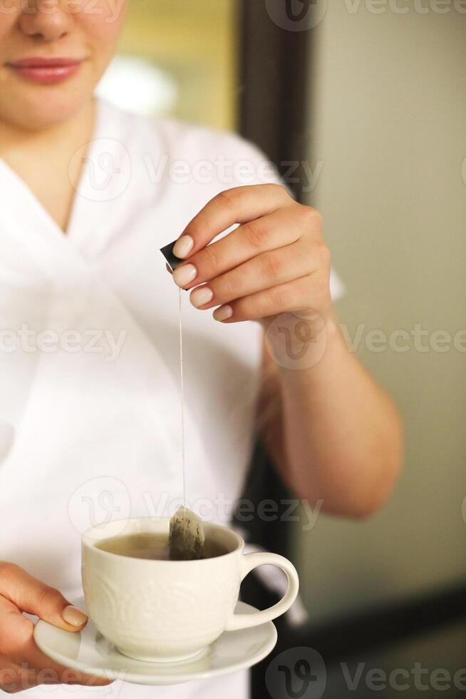 Happy lovely young female health worker laughing sincerely while holding cup of hot tea photo