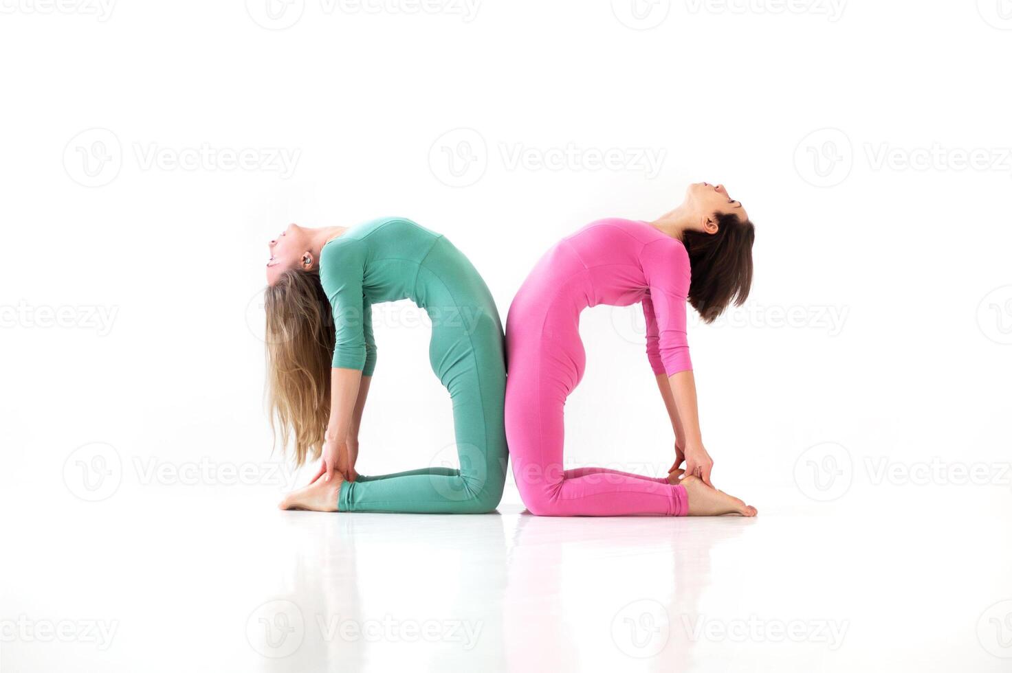 Two young women doing yoga indoor, standing in camel Ustrasana position facing each other photo