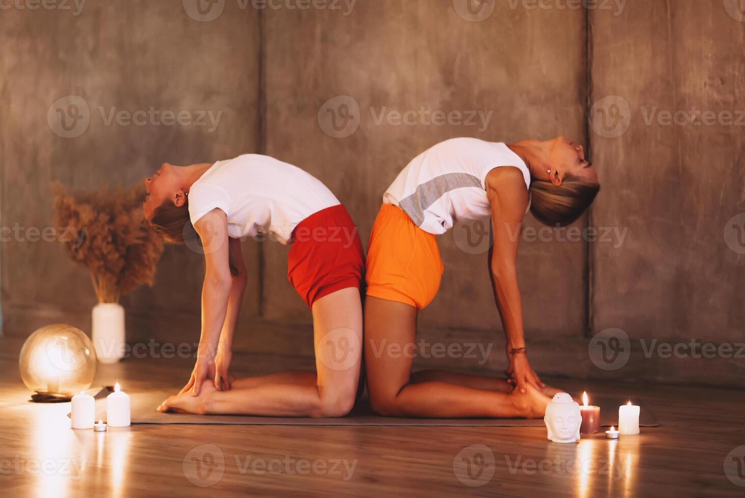 Two young slender woman in colorful sportive wears doing yoga in gym or studio photo