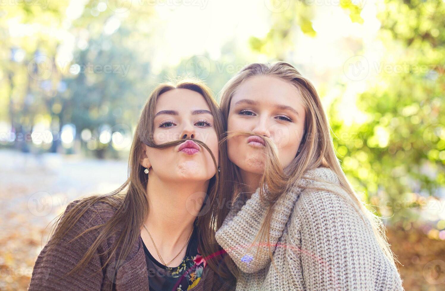 Fashionable beautiful young girlfriends with hairdress together in the autumn park background. Having fun and posing. photo