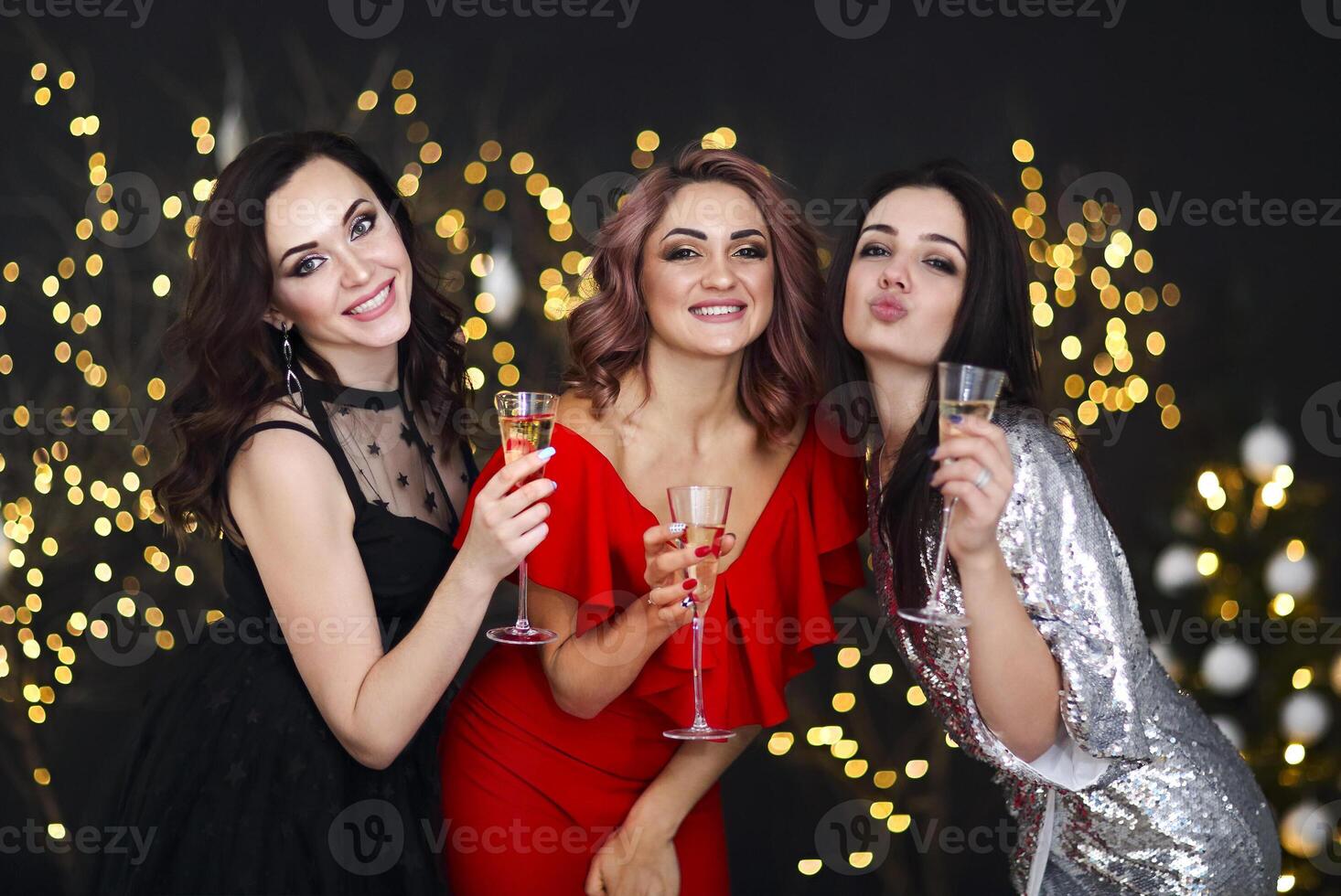 Smiling women in evening dresses with glasses of champagne over lights background photo