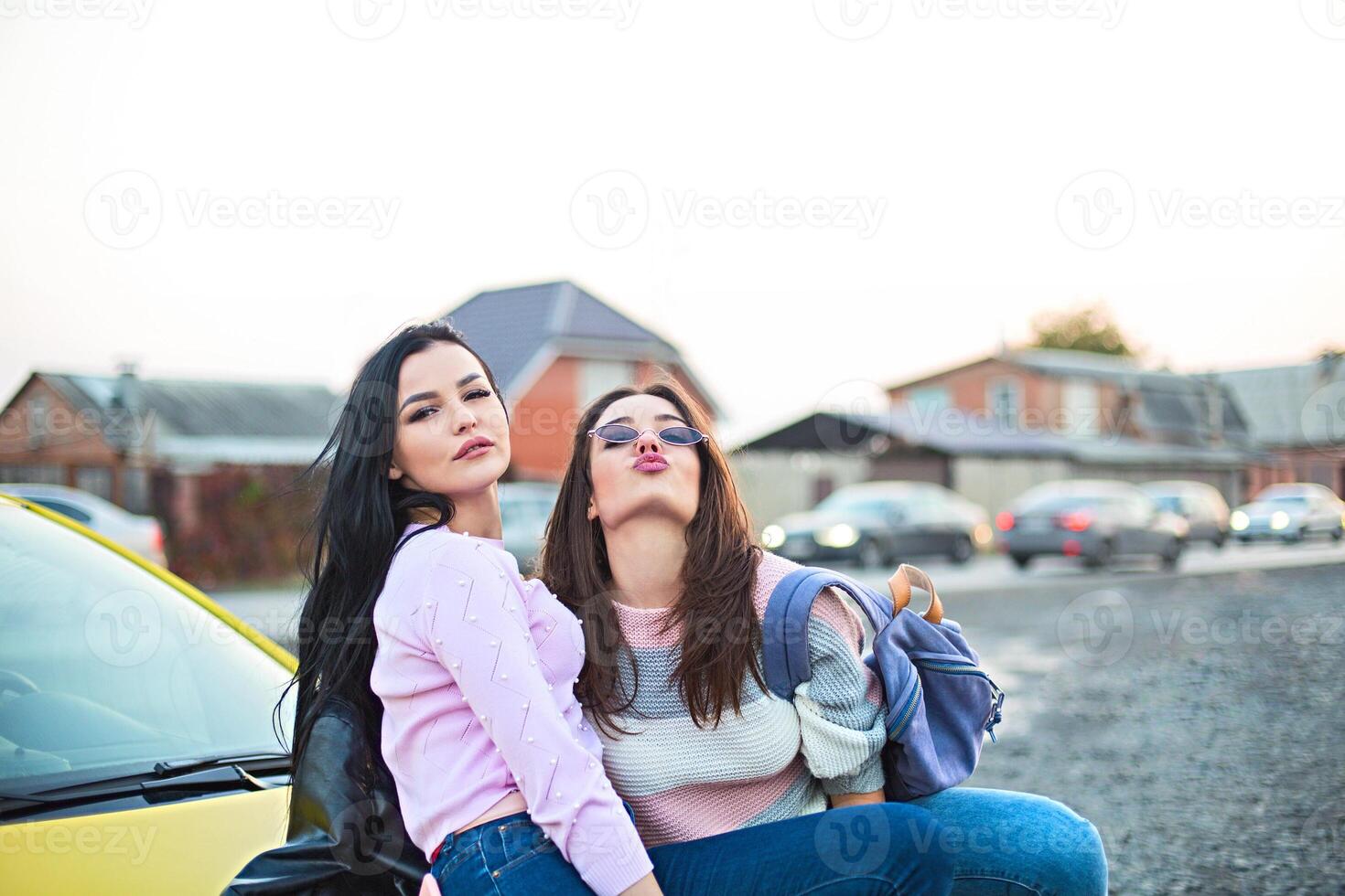 Best female friends cheering by car road trip at sunset. Happy people outdoor on vacation tour photo