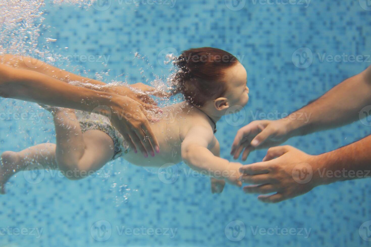 Father and mother teaching small child swimming underwater in the pool photo