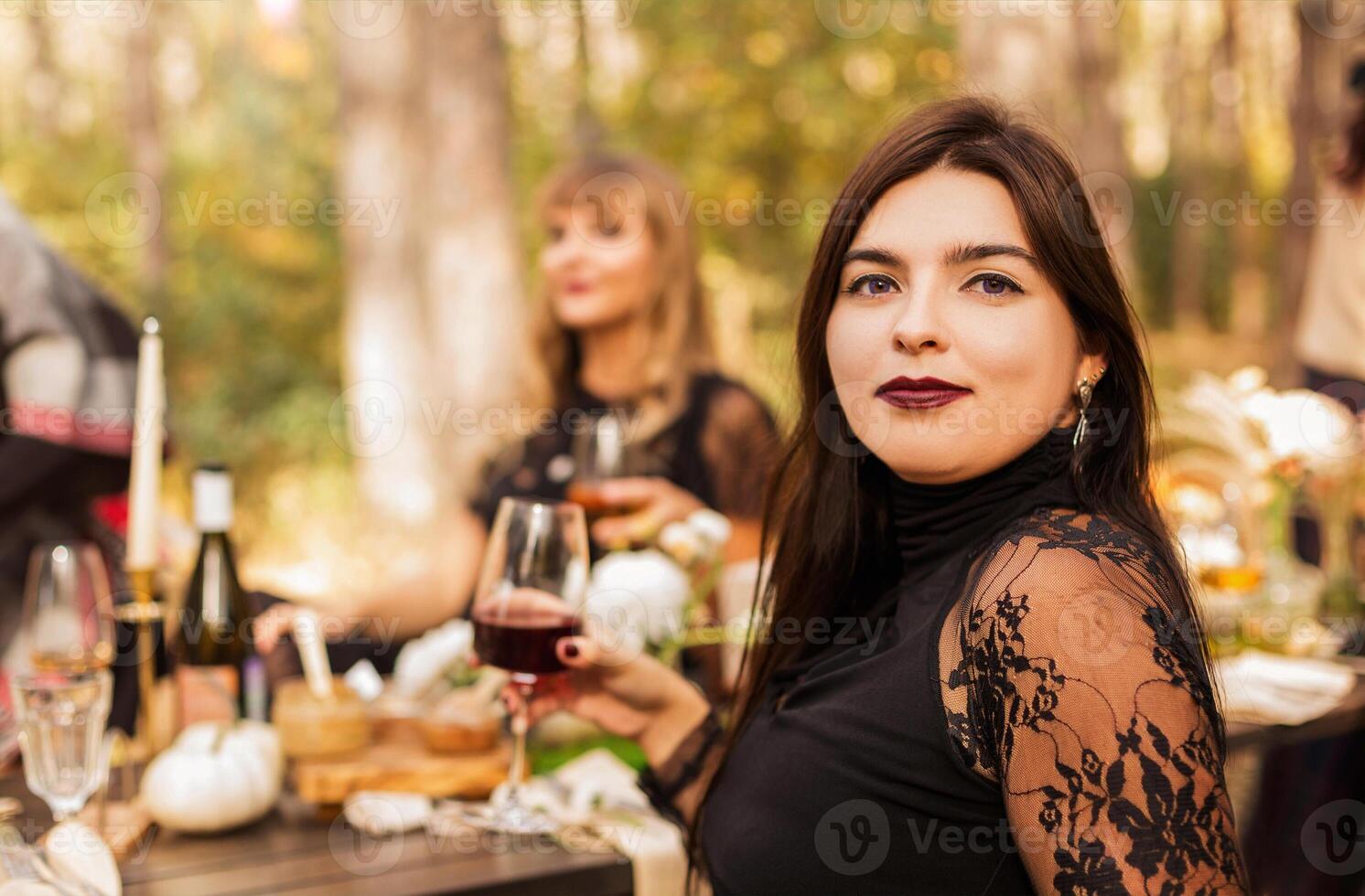 Portrait of beautiful woman with evening makeup in black dress sitting with friends at table outside photo