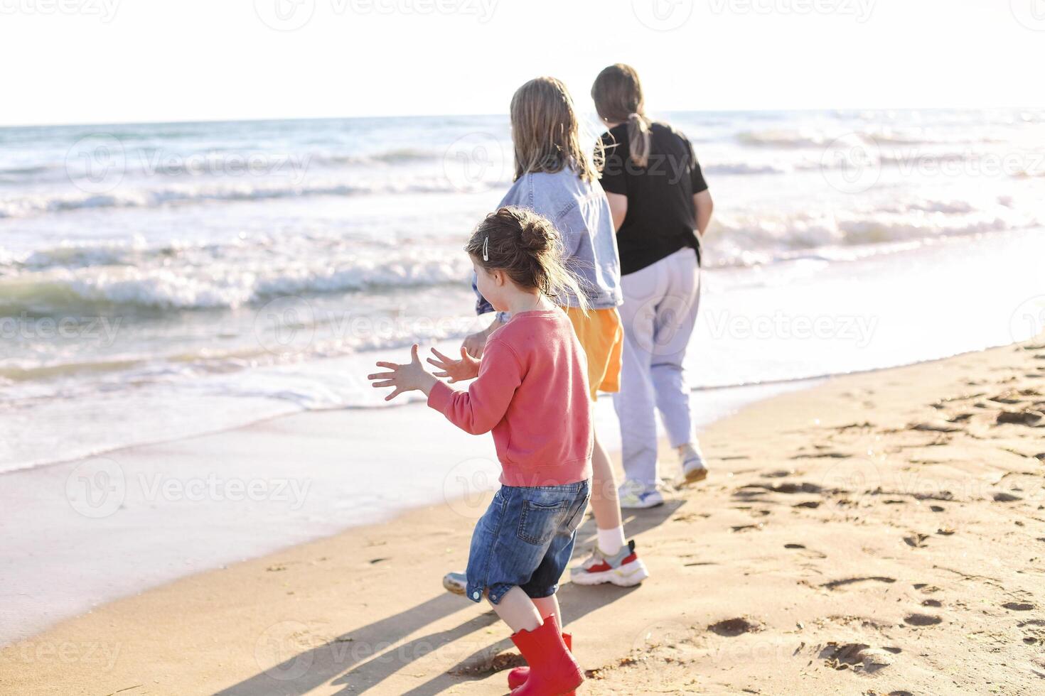 Joyful happy family mother and two daughters standing on seashore looking at surf and waves photo