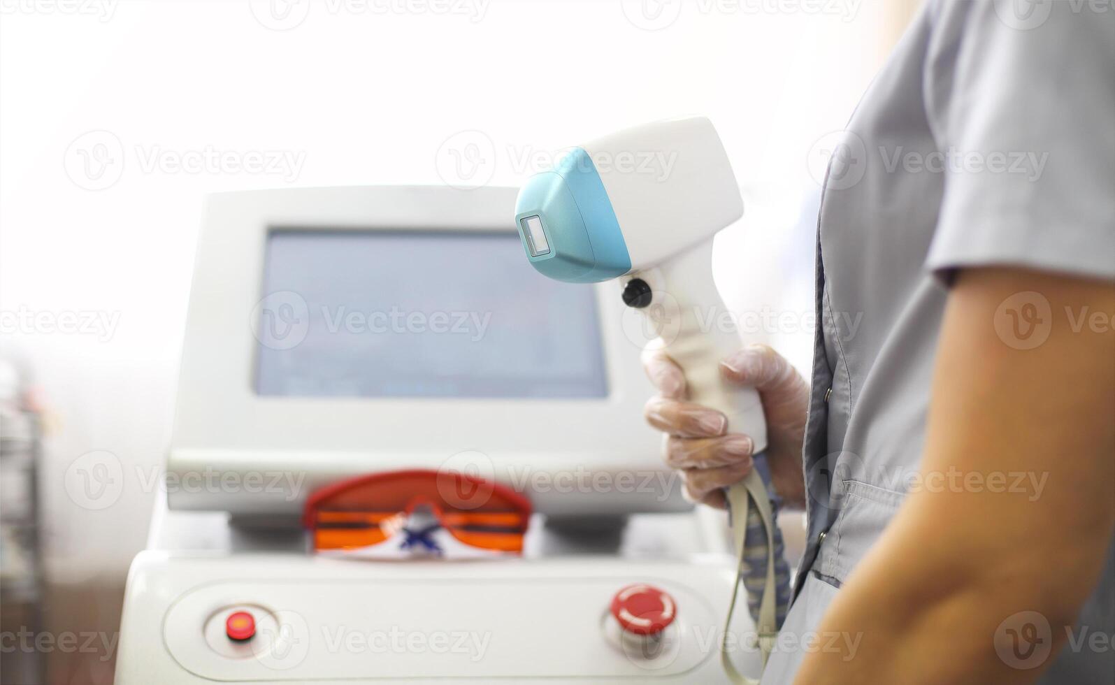 Young woman beautician in medical uniform adjusting machine for photorejuvenation or laser hair removal while waiting for next customer in spa parlor photo