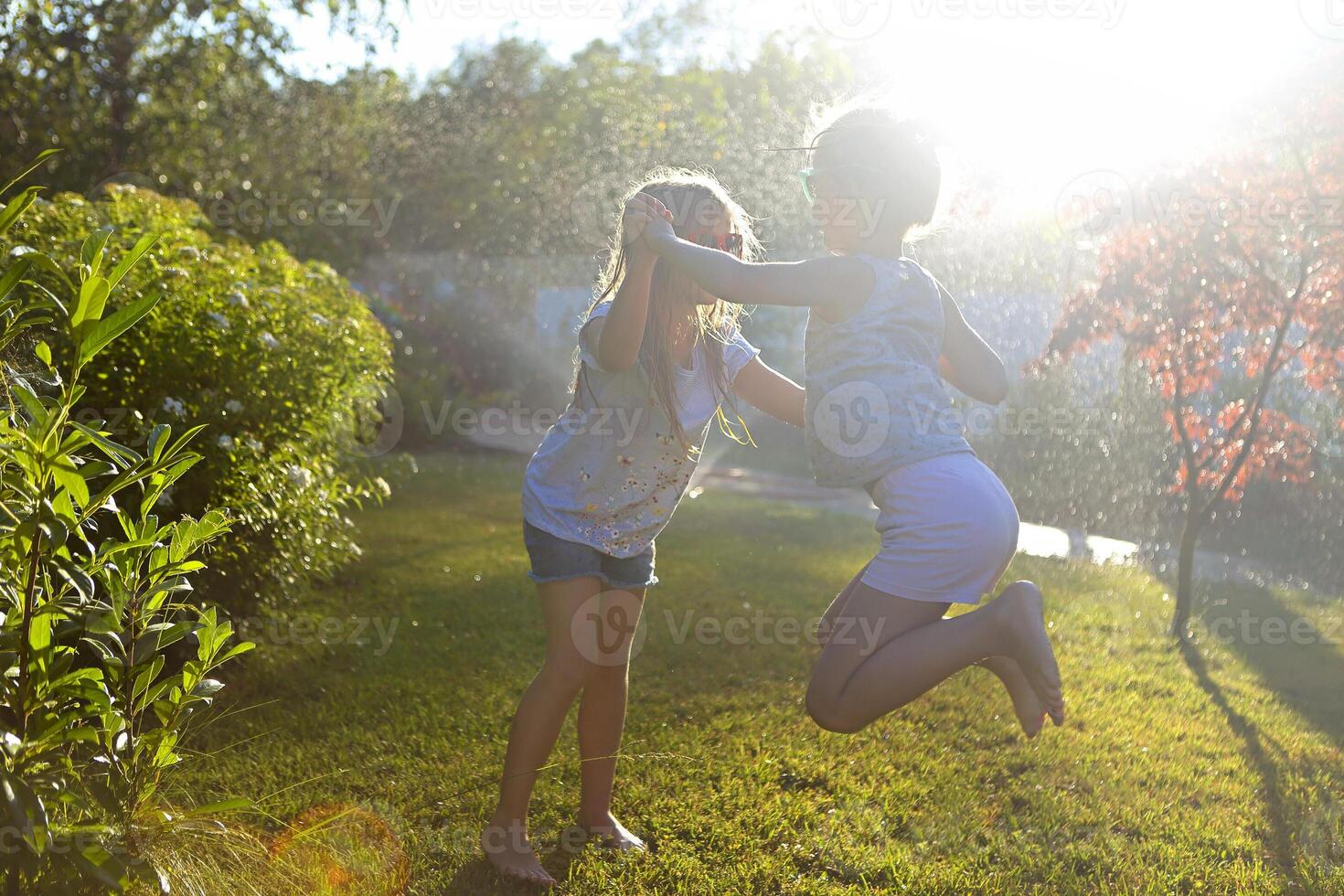 Child playing with garden sprinkler. Kids run and jump. Summer outdoor water fun in the backyard. Children play with hose watering flowers photo