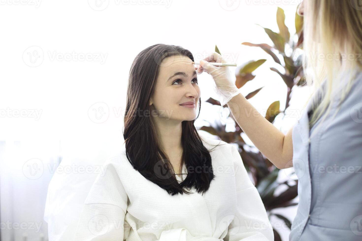Aesthetic cosmetology. Facelift in spa salon. Beautician makes markup for injection. Smoothing of mimic wrinkles photo