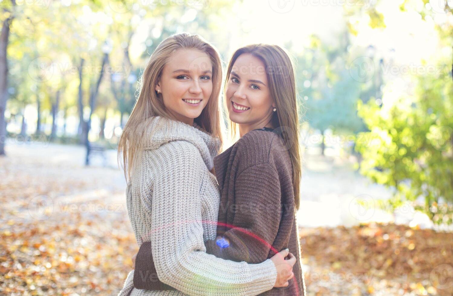 Fashionable beautiful young girlfriends walking together in the autumn park background. Having fun and posing. photo