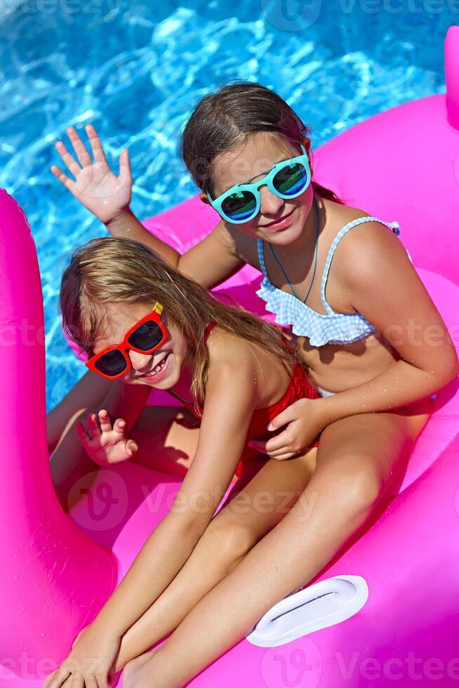 Portrait of two girls wearing sunglasses, happy friends on inflatable flamingo swim float photo