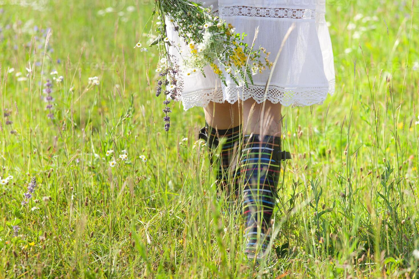Anonymous woman with flowers walking in field photo