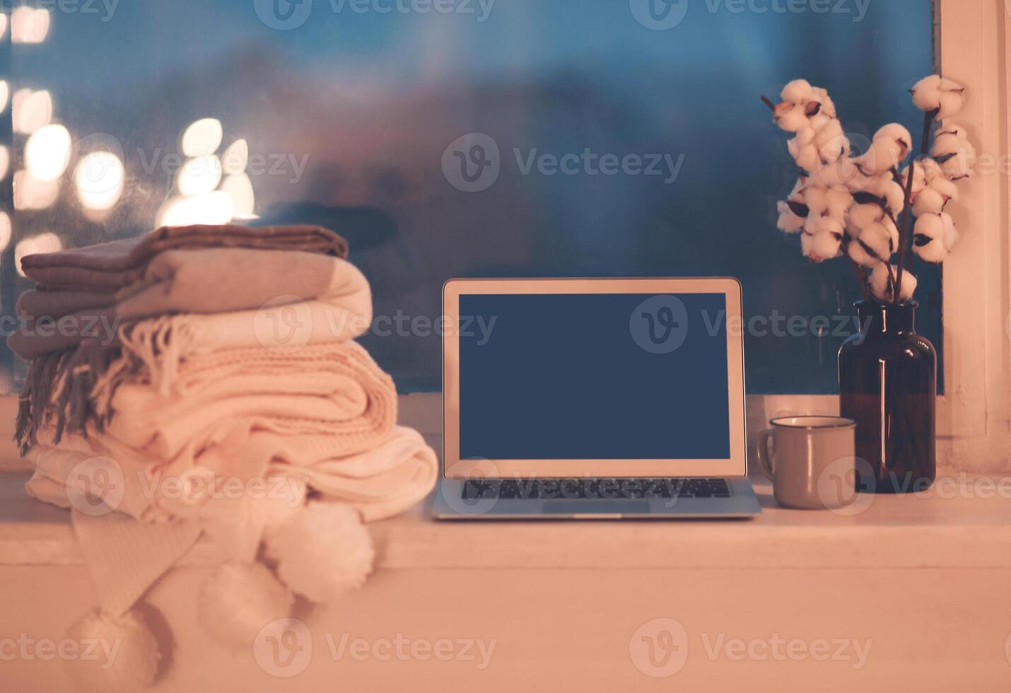 Mug, computer and cozy plaids on window in night photo