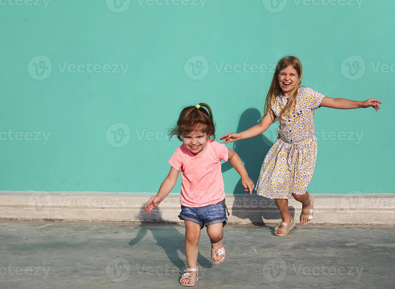 Cheerful little sisters in colorful dresses runing against green wall photo