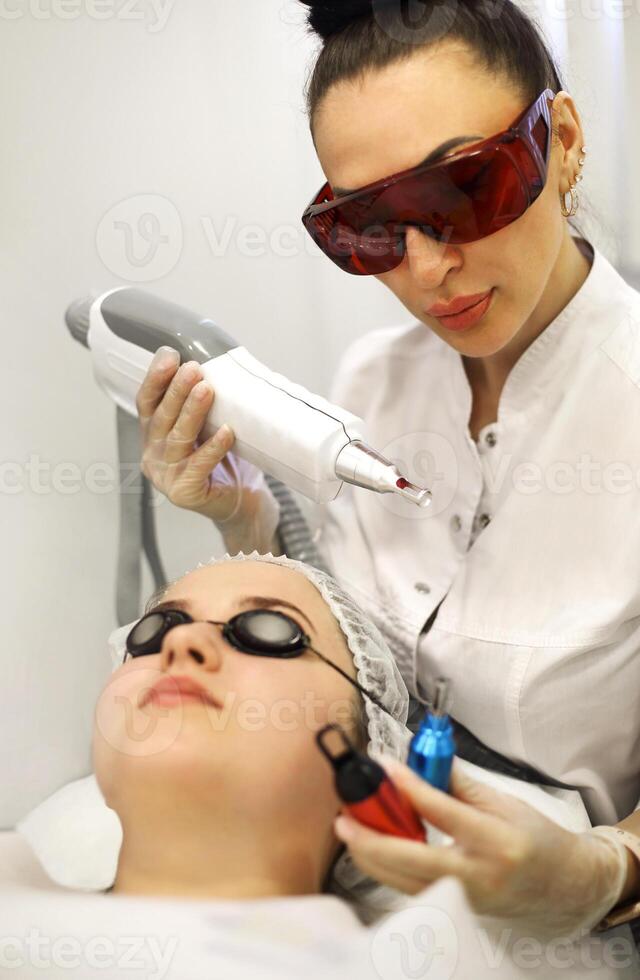 Woman treating client face with laser photo