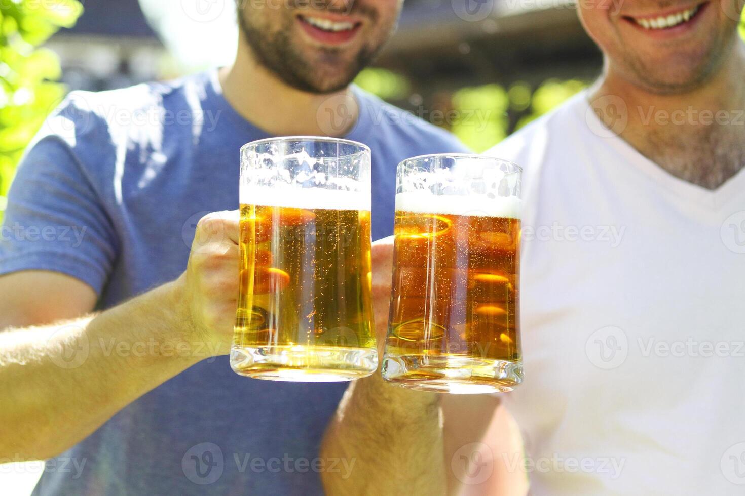 Close up of two young men in casual wear stretching out glasses with beer and smiling photo