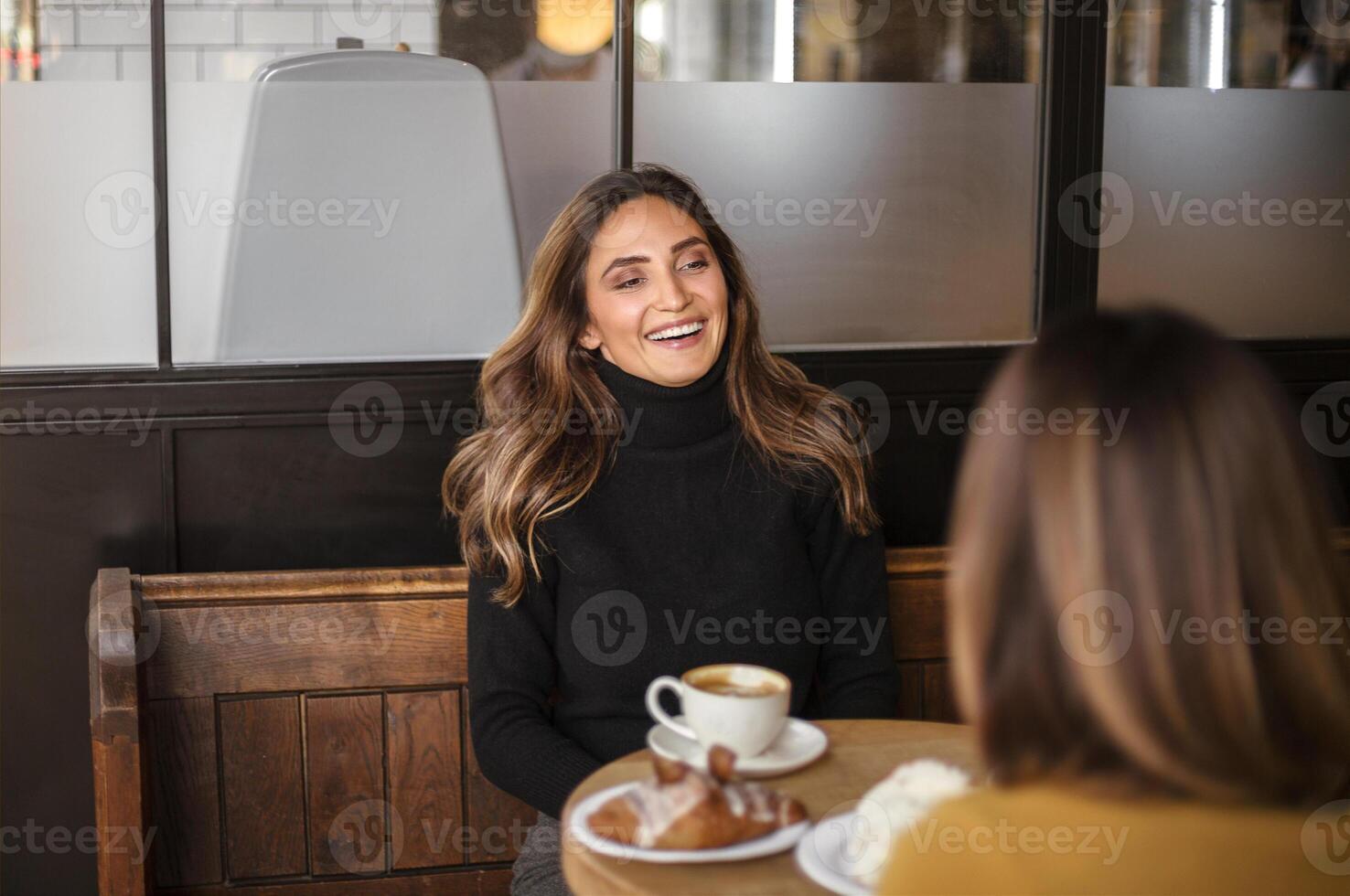 Two delighted women girlfriends drinking coffee and talking during meeting in cozy cafe photo