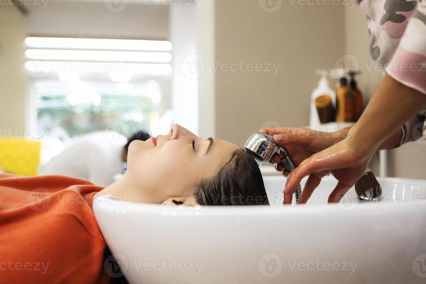 Cheerful young woman enjoying head massage while getting her hair washed by a professional hairdresser photo