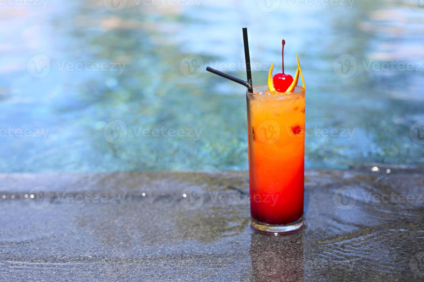 Glass with a bright tequila sunrise cocktail by the pool. photo