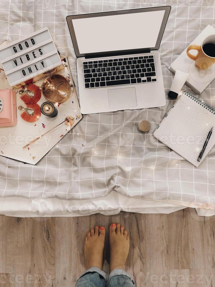 Top view of cozy blogger workplace with mockup laptop, agenda, coffee cup and decorations on bed photo
