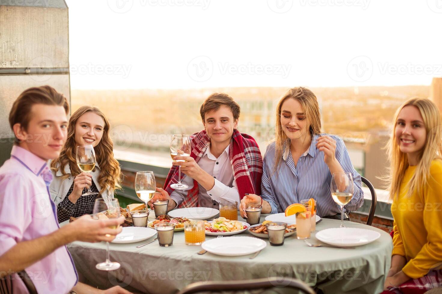 Cheerful friends drinking white wine during roof party photo