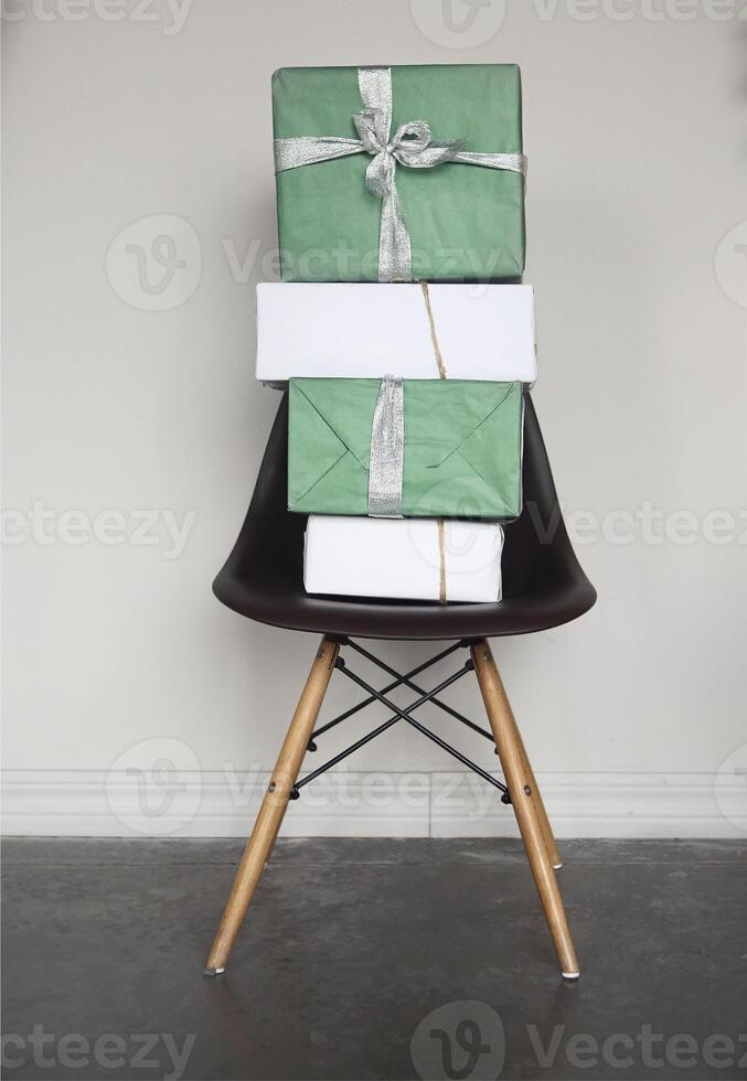 Green and white Christmas gift boxes with red ribbons on chair near grey wall photo