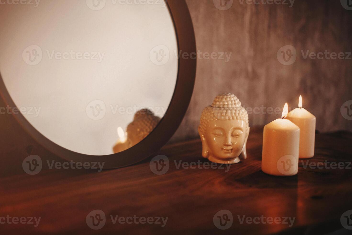 Round mirror on wooden shelf with two burning candles and small porcelain Buddha head photo