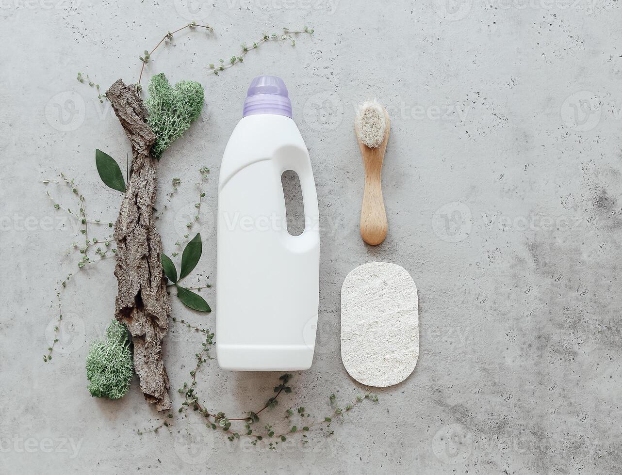 Composition with bottle of laundry detergent by tree bark, tiny mosses and grass on light concrete background photo