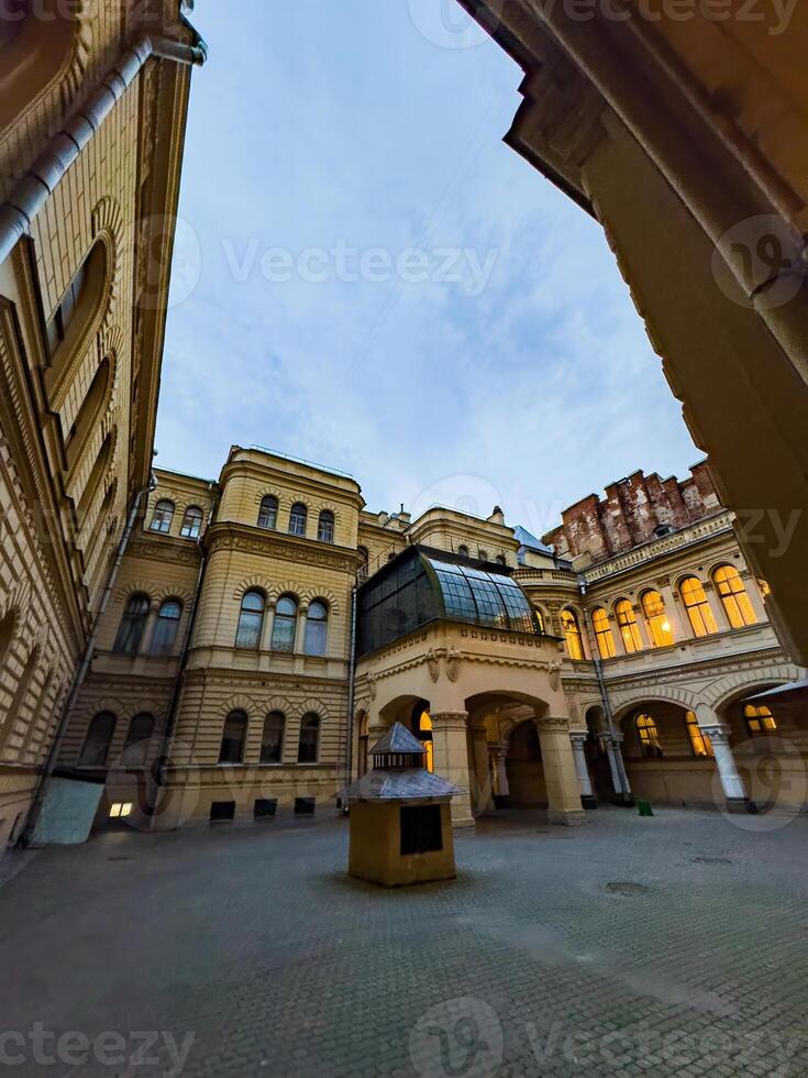 A view of a historic courtyard with elegant architecture illuminated by warm lights at dusk. The image captures the intricate details of the buildings, showcasing the blend of old-world charm and architectural beauty. photo