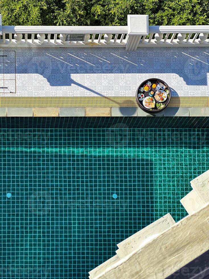 Top-down view of a delicious breakfast served poolside at a luxurious pool, showcasing the beautiful tiled design and vibrant greenery, perfect for themes of luxury living and relaxation photo