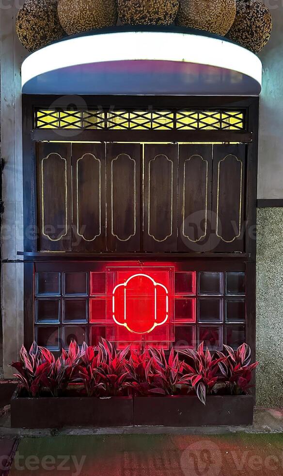 A beautifully designed entrance with traditional Asian wooden panels, a vibrant red neon light, and lush plants, creating an inviting and stylish ambiance, perfect for restaurants or themed venues photo