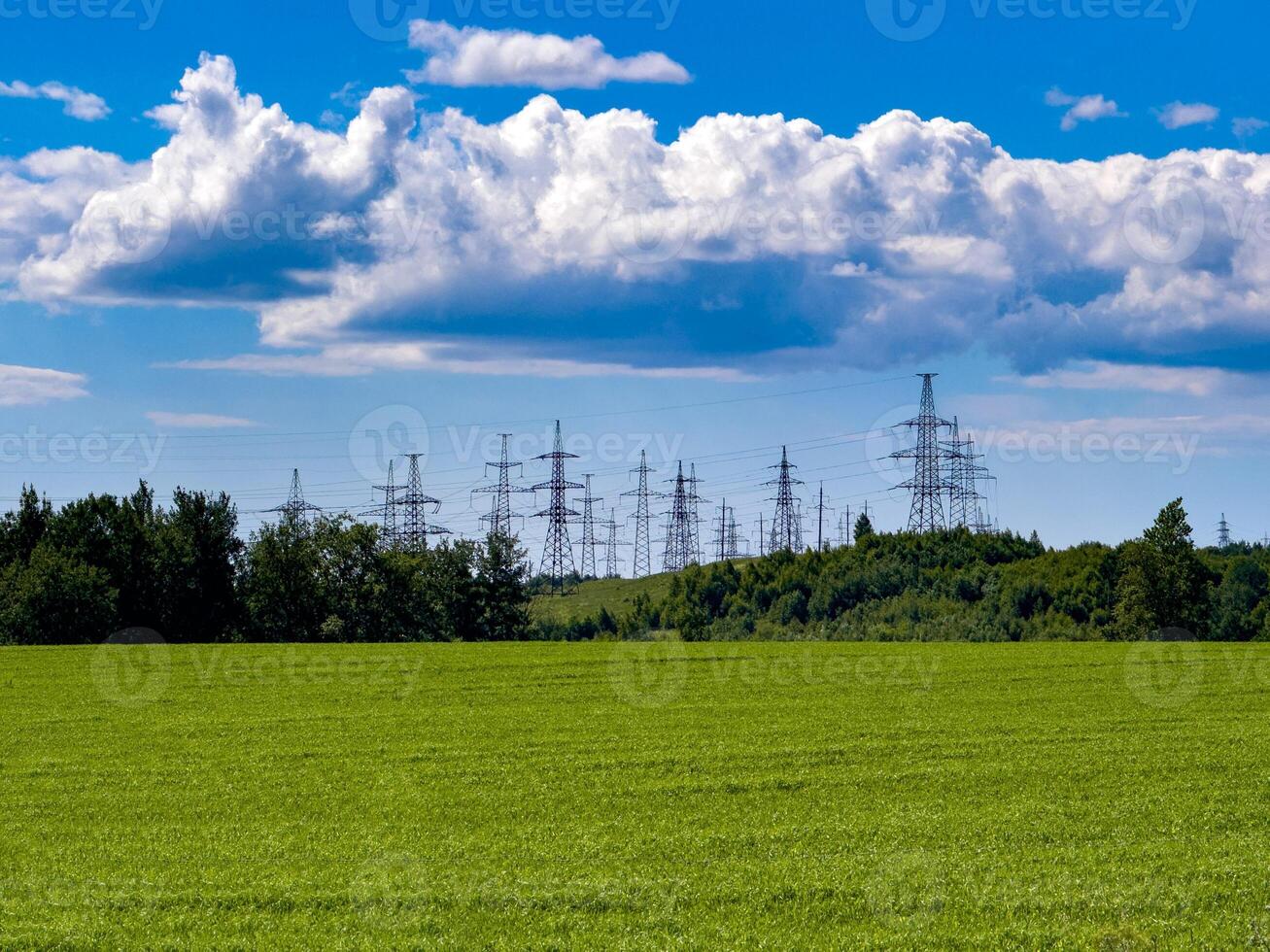 An image featuring high voltage power lines stretching across a lush green countryside under a clear blue sky. Perfect for showcasing the balance between technology and nature photo