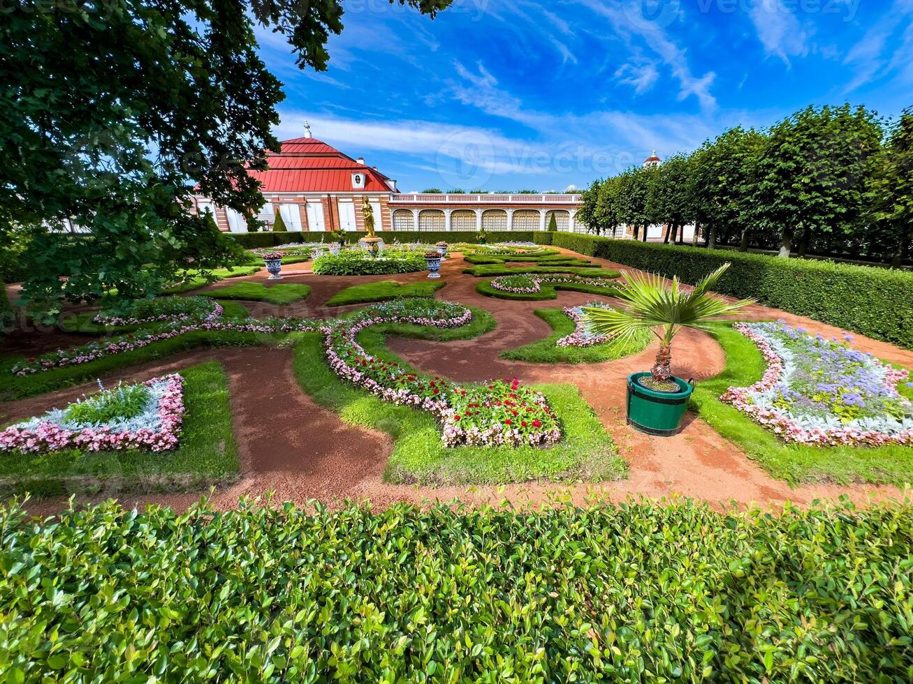 Vibrant view of a meticulously manicured garden featuring colorful flower beds and ornamental plants, surrounded by lush greenery and set against a bright blue sky, perfect for a peaceful stroll photo