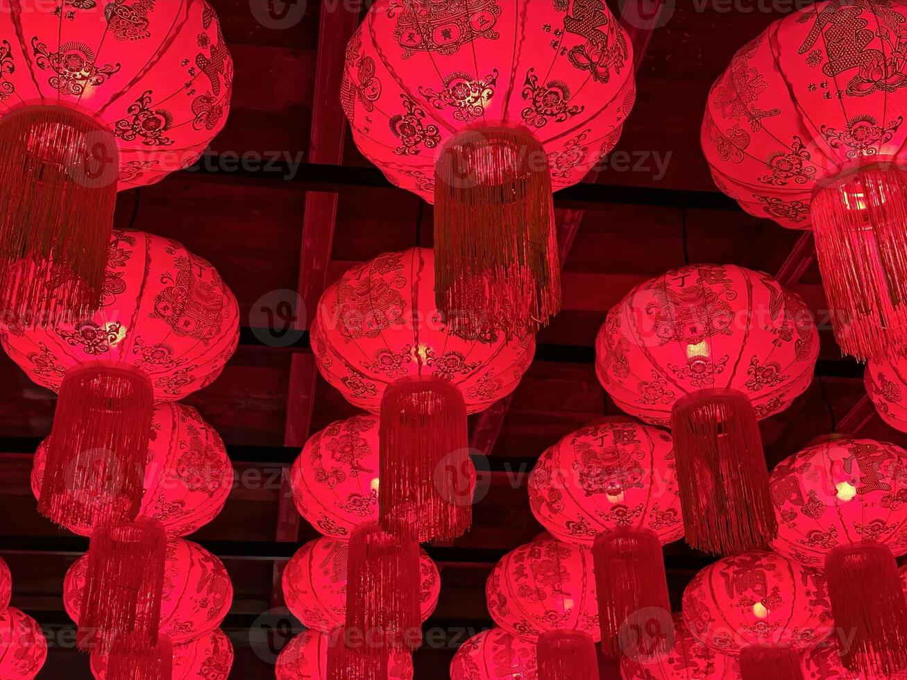 Close-up of traditional red Chinese lanterns with intricate patterns and tassels hanging from a ceiling, illuminated to create a warm festive ambiance, perfect for celebrating Chinese New Year or other cultural events photo