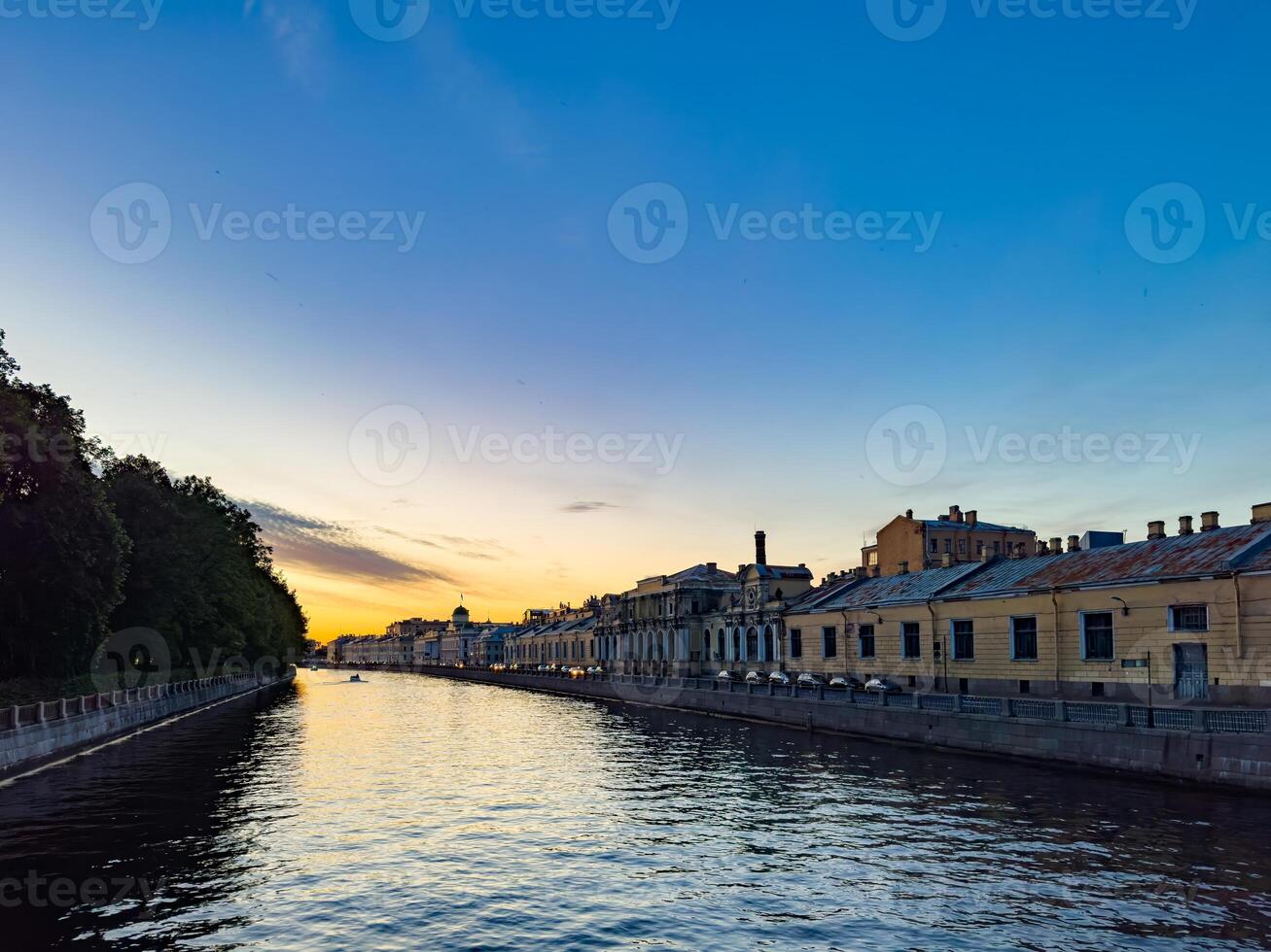 A tranquil scene of a canal in St. Petersburg, Russia, captured at sunset. The calm water reflects the colorful sky, while historic buildings line the canal, creating a picturesque and peaceful evening view photo