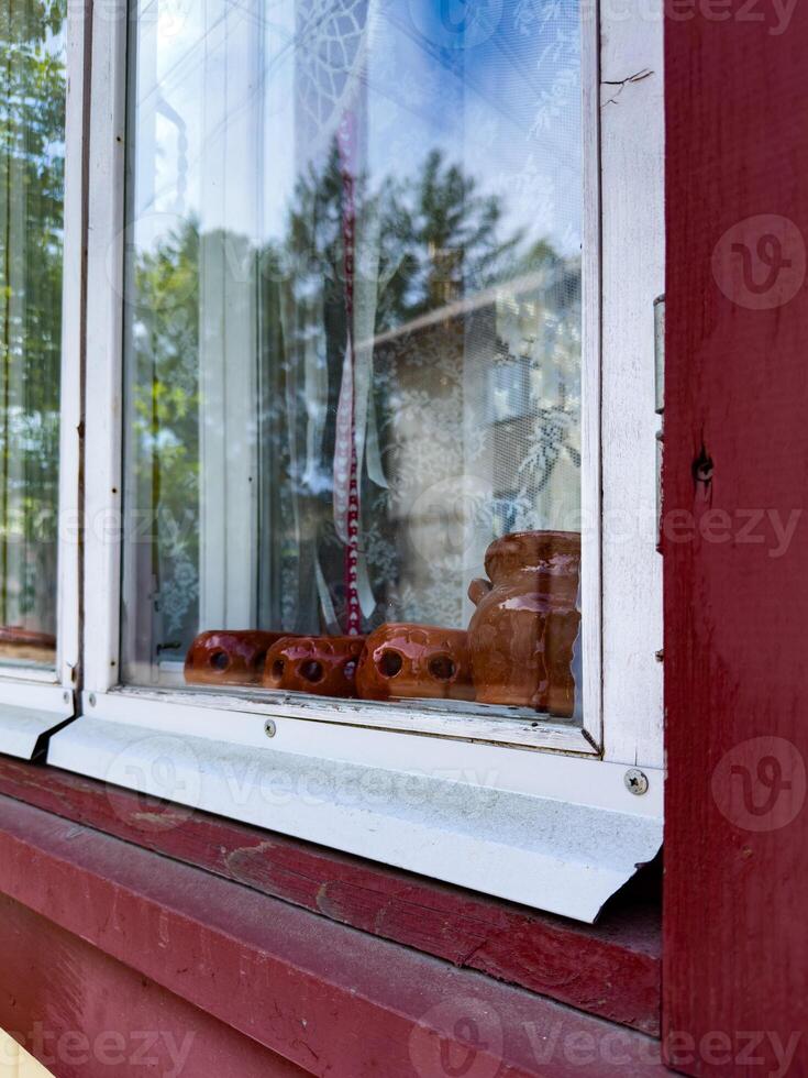 A close-up view of a rustic window adorned with clay figurines and delicate lace curtains, offering a glimpse into a cozy, traditional home atmosphere photo