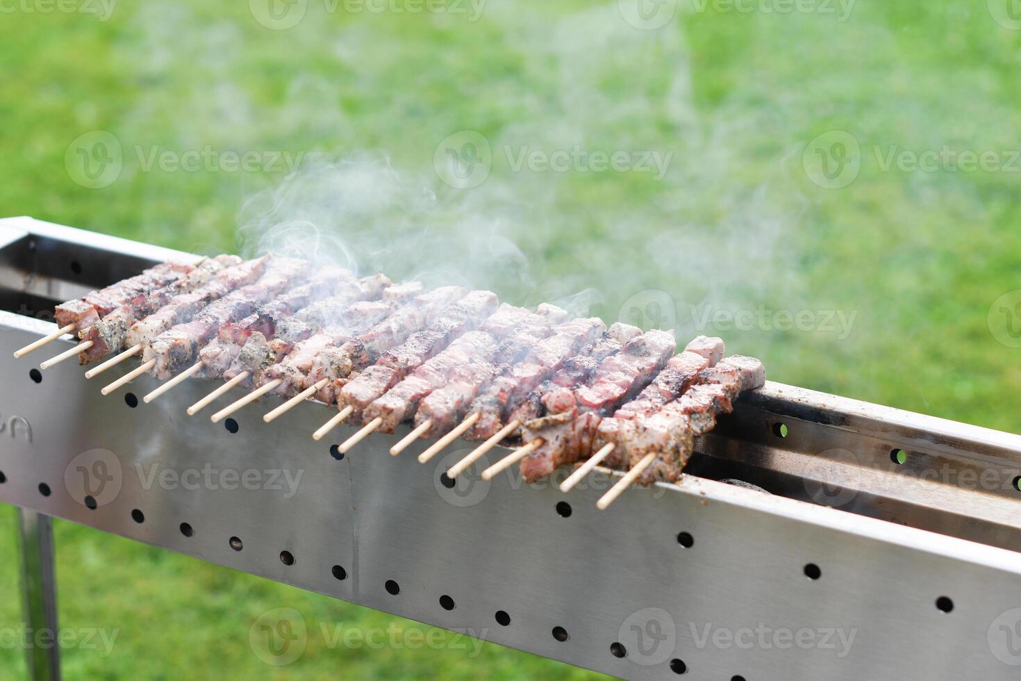 a young man grills meat kebabs on coals, ARROSTICHINI - typical southern Italian cuisine, a luxurious picnic on the terrace near the house in the summer, aromatic smoke rises above the barbecue, photo