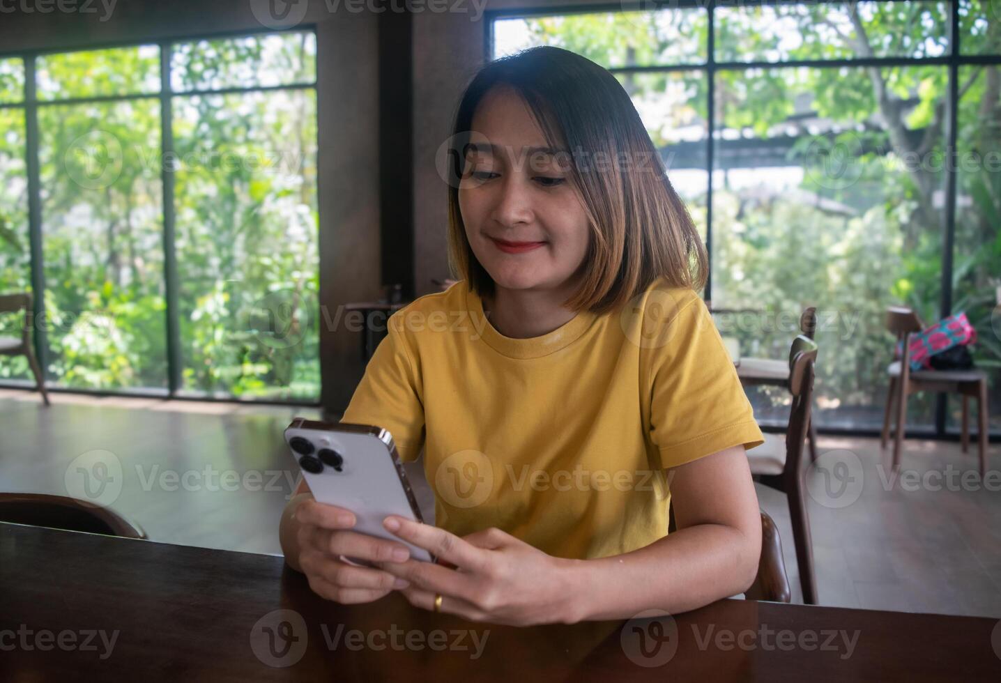 Asian woman sitting on chair in the cafe,wearing round neck shirt orange holding using phone watching and reading something with happy smiling. photo