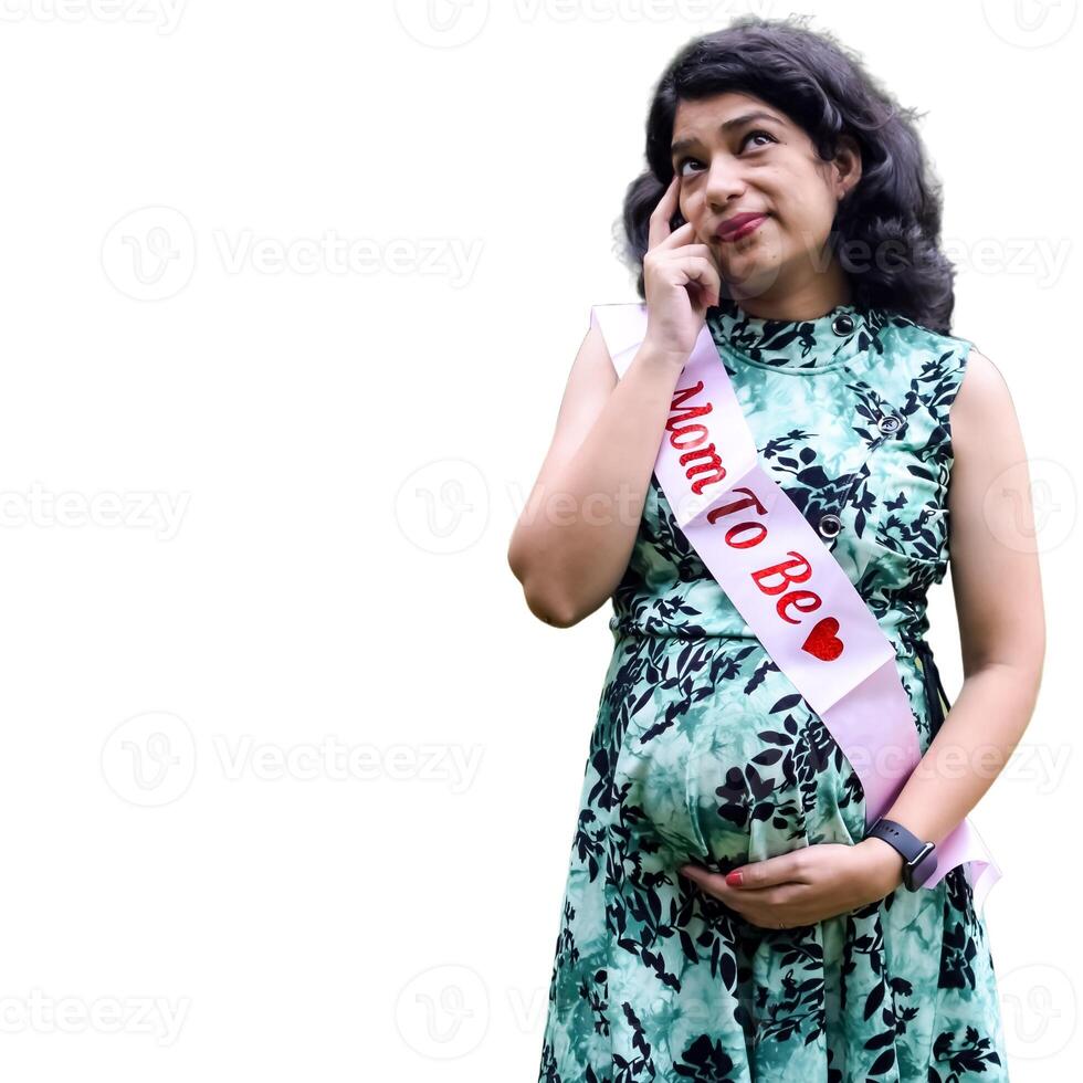 A pregnant Indian lady poses for pregnancy shoot and hands on belly with white background, Indian pregnant woman puts her hand on her stomach in maternity dress with plain background, Pregnancy shoot photo