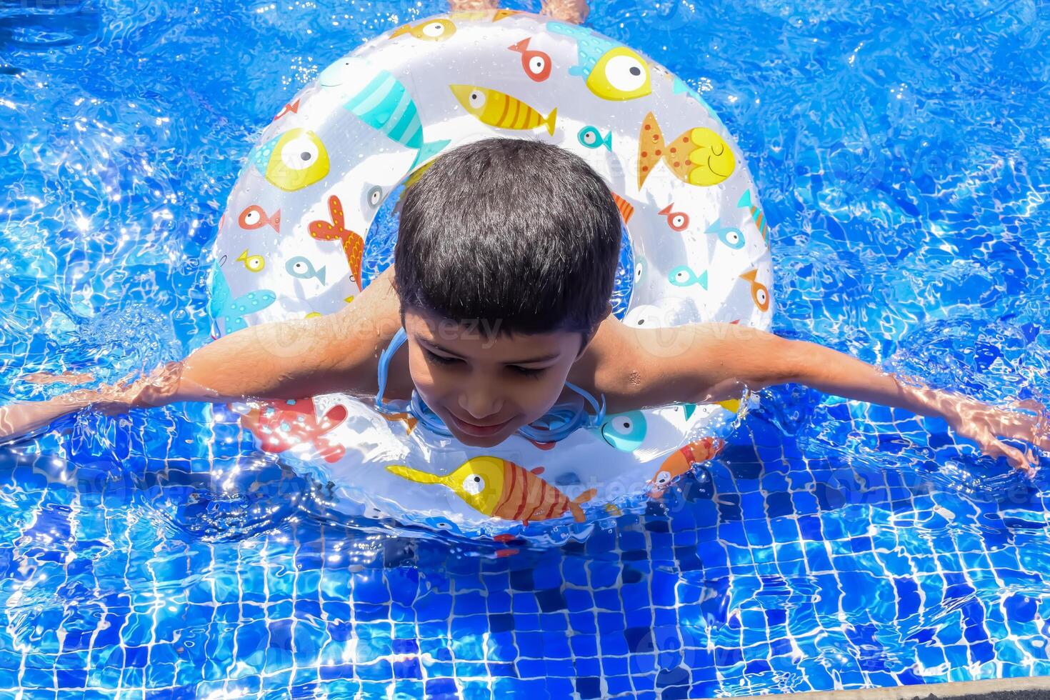 Happy Indian boy swimming in a pool, Kid wearing swimming costume along with air tube during hot summer vacations, Children boy in big swimming pool. photo