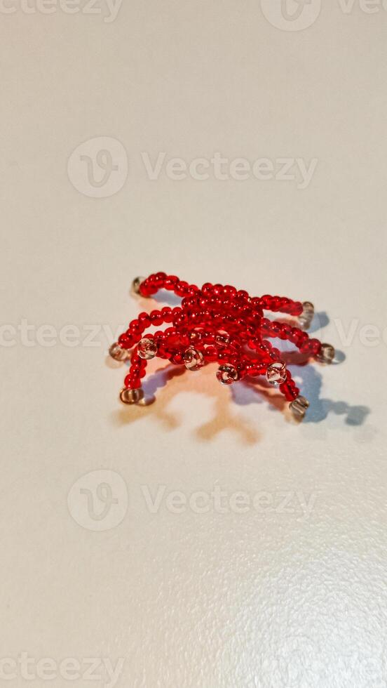 A small, intricate crab made of red beads rests on a surface photo