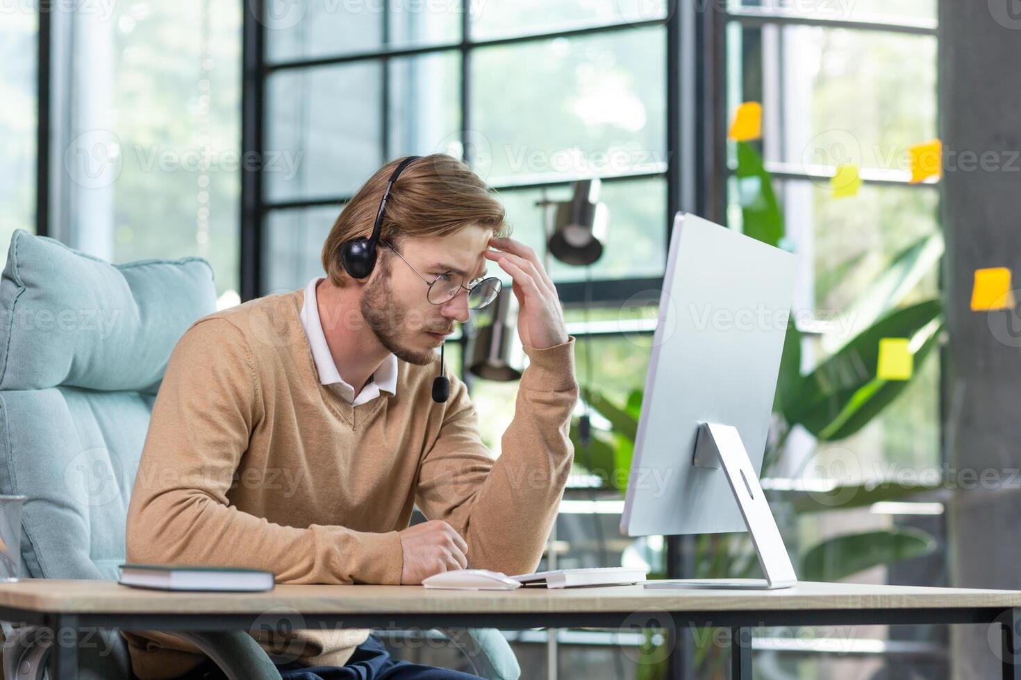 Tired worker in headset holding hand to head, sitting at table, suffering from headache, tired from work wants to sleep. photo