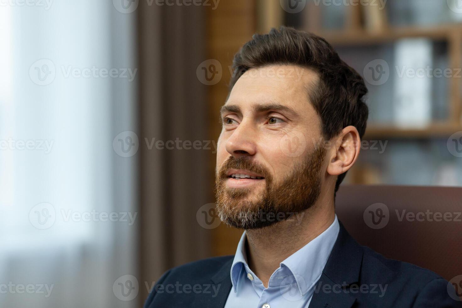 Confident caucasian man with trendy hairstyle looking ahead inspired on blurred background. Satisfied male boss listening to quarterly report with impressive results from hired employee in cabinet. photo