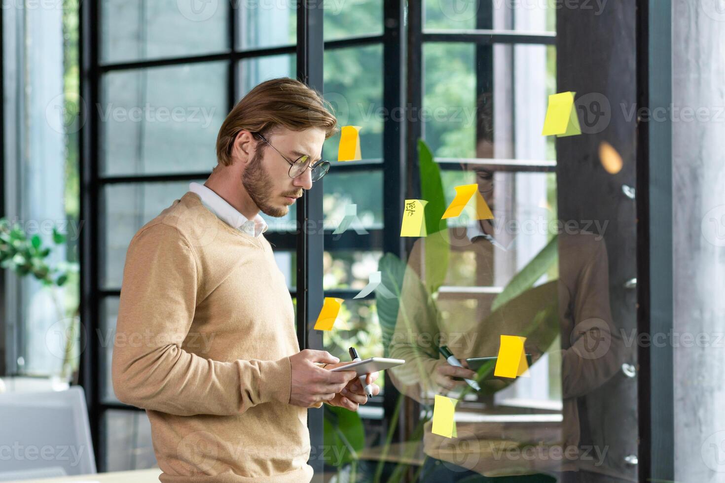 Portrait of a young programmer standing in the office near a glass transparent board and working with concentration on a tablet. Planning, developing, typing. photo