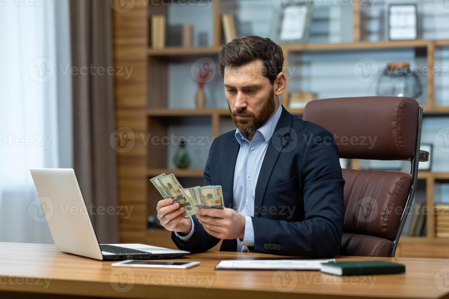 Concentrated and serious young man businessman sits in the office at the desk and counts cash money. Received salary, income, bribe. photo