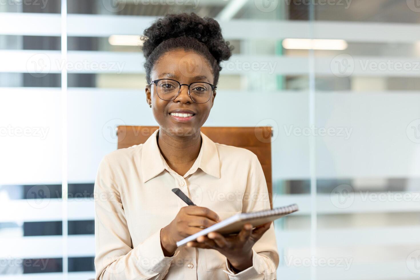 Confident businesswoman holding pen and notebook during call in modern office. Smiling professional taking notes, demonstrating engagement and readiness. photo